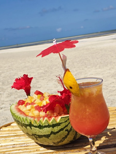 Tropical fruit bowl and cocktail on white sand beach